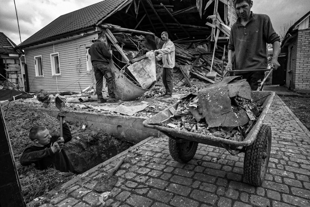A man hauls debris from a damaged house in a wheelbarrow