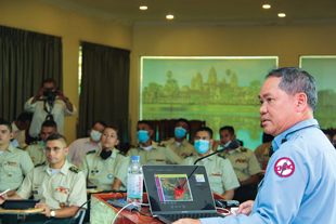 A man with a laptop presents to a room full of uniformed people.
