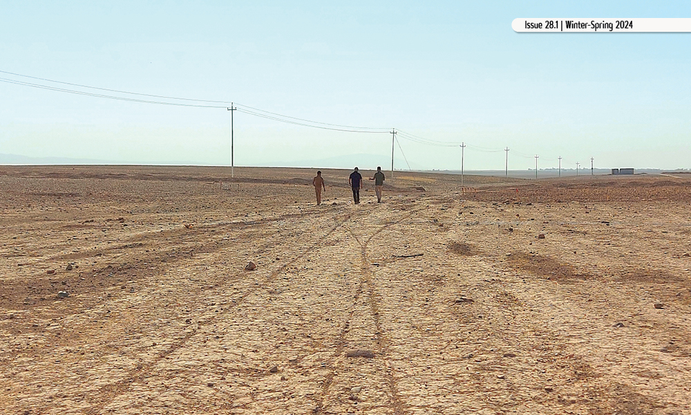 Three people walk across cracked ground with power lines visible in the distance.