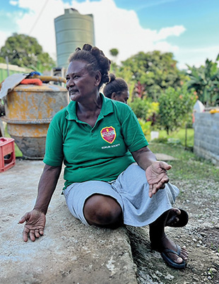 A woman in a green shirt sit on the ground with open hands.