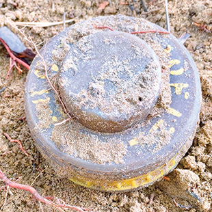 A circular, plastic, dirt-covered mine with yellow writing.