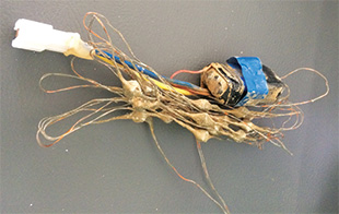 A bundle of wire and cord attached to a dirty battery wrapped in blue tape.