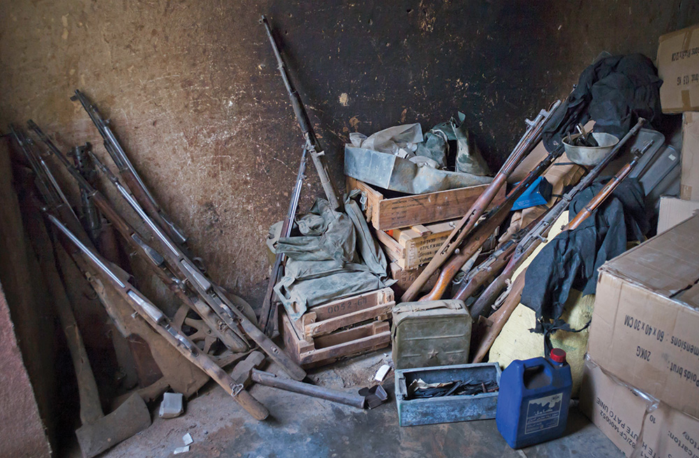 A collection of rusty, old weapons and ammunition against a wall.