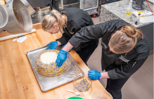 Two students decorating a JMU themed cake.