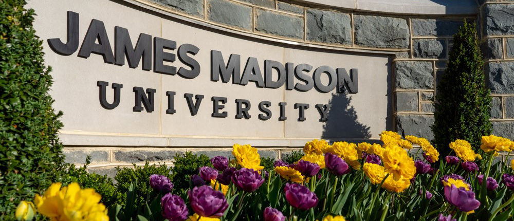 Closeup of JMU sign with bright yellow and purple flowers in foreground