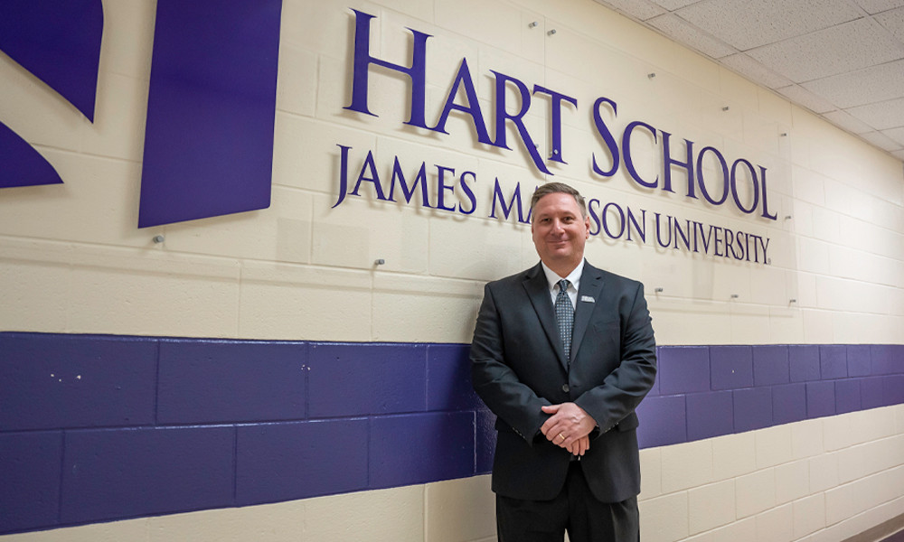 The newly named director of the Hart School, David Shonk, stands in front of a Hart School sign in the hallway.