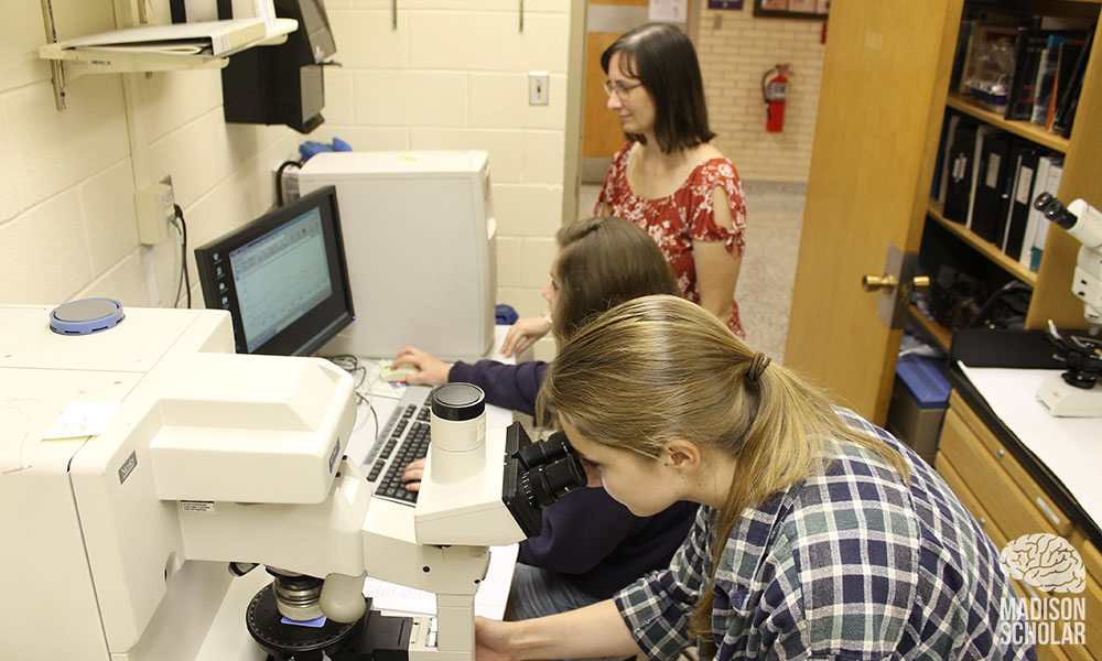 Johson with her students in a lab looking at a microscope and a computer screen.