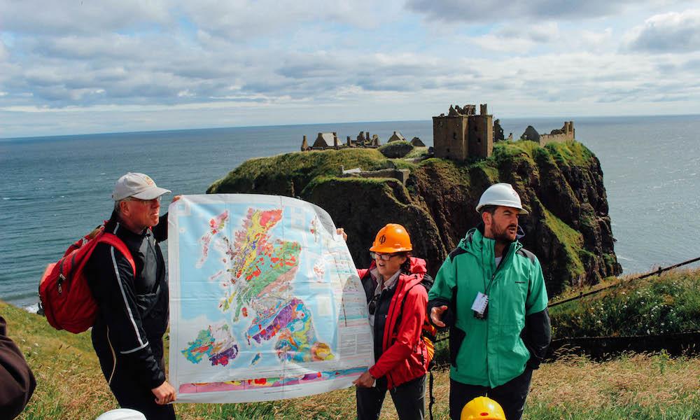 Three individuals studying a map with Scottish castle in background