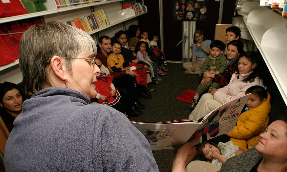 Photo of Pat Kennedy reads a story at a neighborhood bus stop. 