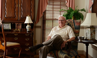 Dr. Clive Hallman seated in chair in his home office