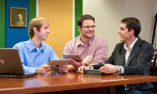 Three students around a table with iPads and laptop