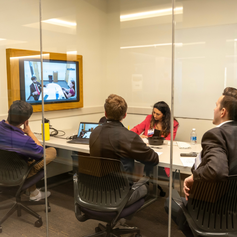 Students sit in a conference room with on a video call.