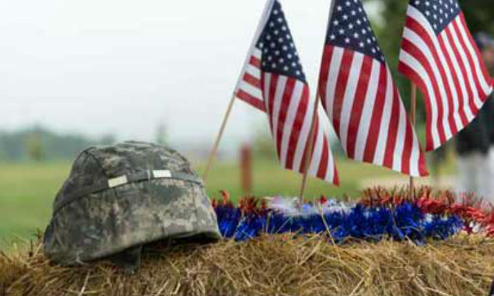 Three small US flags planted beside a military camo cap