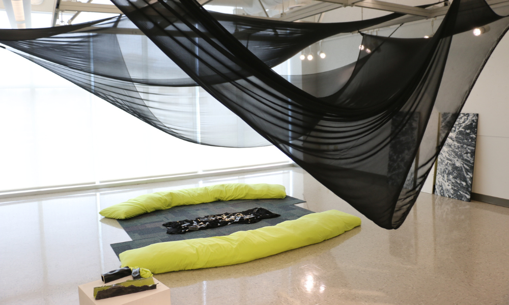 Long green pillows with carpet on the floor with black fabric draped from the ceiling