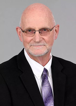 A portrait of Roger Soenksen, in a black blazer with a purple tie.