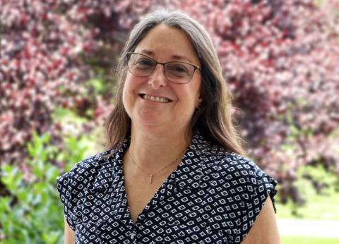 A portrait of Dianne Fulk, smiling while standing in front of colorful trees.