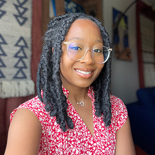 A portrait of Courtney Murray Ross, with clear-frame glasses and medium-length dark hair in twists. 