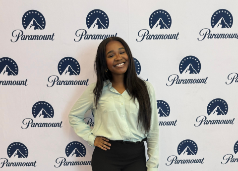 Sheridan Osei, a young Black woman, stands in front of a backdrop of Paramount logos.