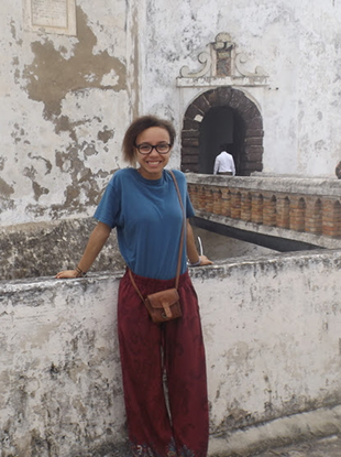 Yasmine Vaughan leans against a low law in front of a tall, white-washed building.