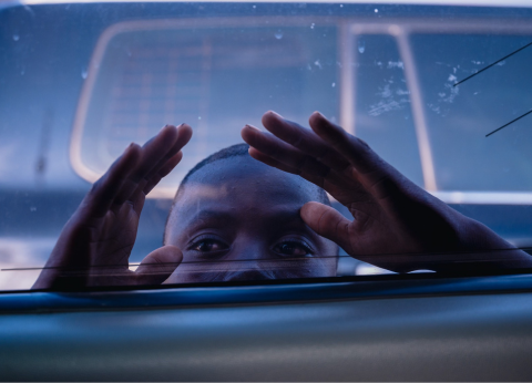 A young African child peers through the window of a car.