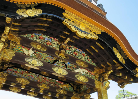 An elaborately painted and gilded arch under a blue sky. Karamon Gate at Nijo Castle.