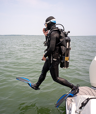 A person in full scuba gear stepping off a boat into blue-green water.