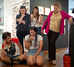 Five people gathered around a camera on the floor, some sitting and some standing.