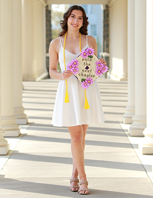 A woman in a white dress poses with a graduation cap that says "onto the next chapter"