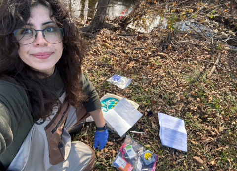 A young person takes a selfie of themselves and several pieces of paper and tools spread on the ground in front of them.