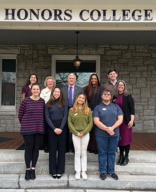 Ai Vy Le stands in a group in front of the Honors College building alongside fellow students and former university president Jonathan Alger.