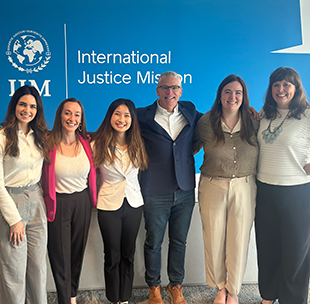 A group of six people standing in front of a blue wall that reads International Justice Mission.