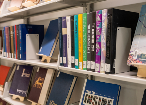 A display of a series of yearbooks. Each has "The Bluestone" followed by the year they were published on the spine.