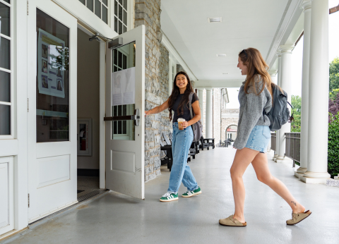 A young woman holds a door open for another person.