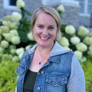 A woman wearing a jean jacket, standing in front of blooming hydrangeas.