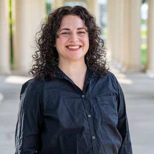 A woman with curly brown hair wearing a dark button-up shirt.