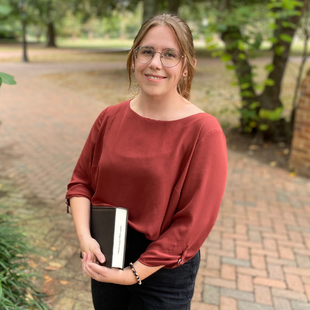 A woman in an orange shirt, holding a book.