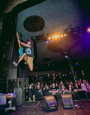 A man with a guitar leaping in the air on a stage during a concert.