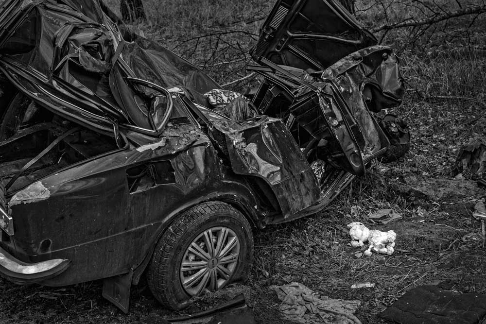 A stuffed animal lies on the ground beside a destroyed car.