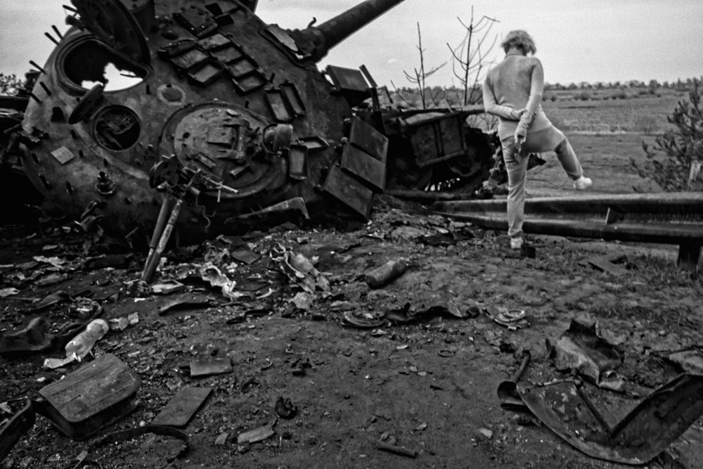 A woman walks over a destroyed tank.