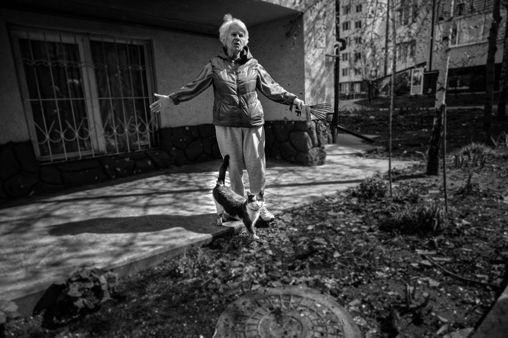 A woman stand in front of her damaged home with her cat.