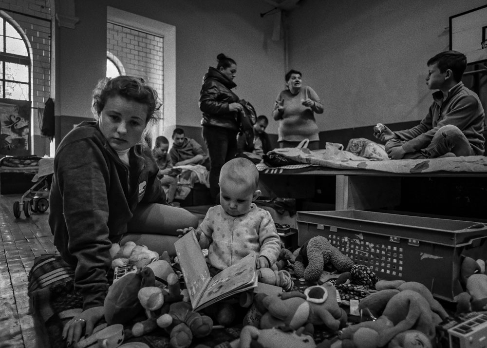 A woman sits on the floor of a train station with a toddler holding a book