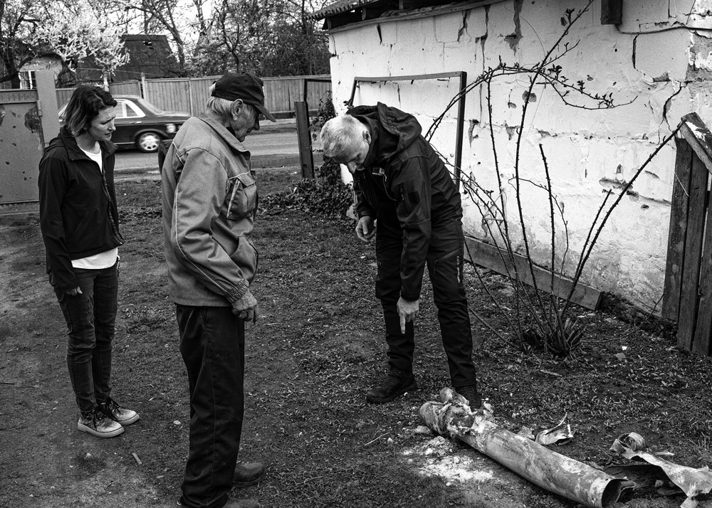 A man points to an unexploded rocket and warns two other people not to touch it.