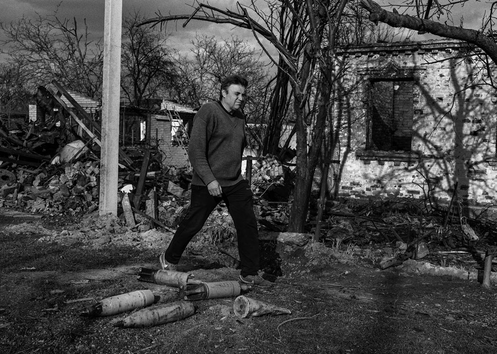 A man walks by bombed out buildings and unexploded projectiles