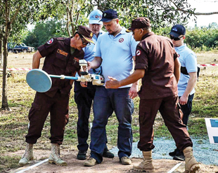 A group of men in brown uniforms gather around a man holding a metal detector.