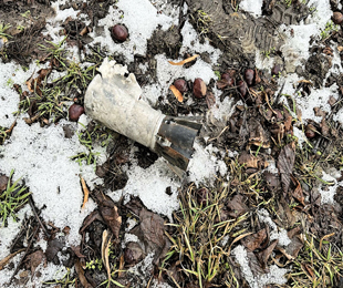 A white cylinder with gray wings on the bottom lying on snowy grass