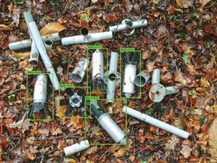 Several pieces of submunitions lying on the ground with small green rectangles around five of them