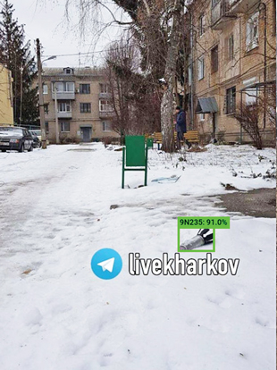 A submunition lying near an apartment complex with a green rectangle superimposed above it/