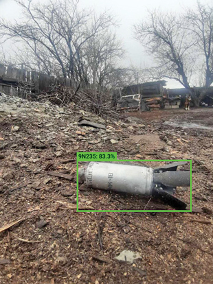 A submunition lying on the ground with a superimposed green box around it.