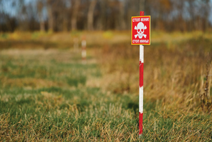 A red sign with a white skull and crossbones that says "Danger Mines" in Ukrainian.