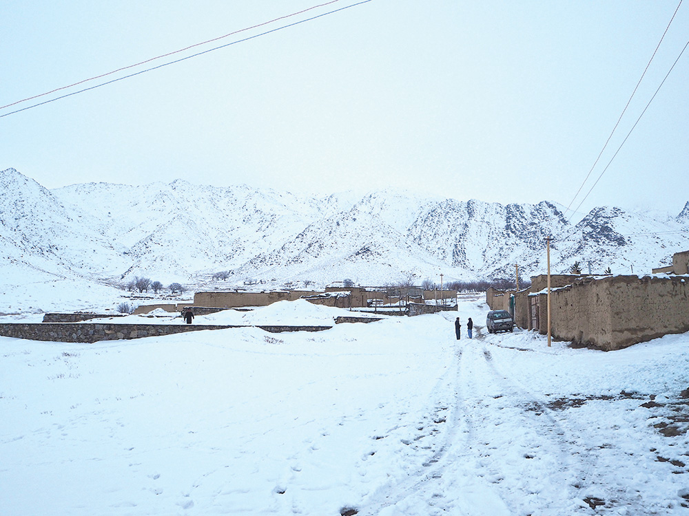 A view of a rural village of clay houses with snow covered mountains in the background